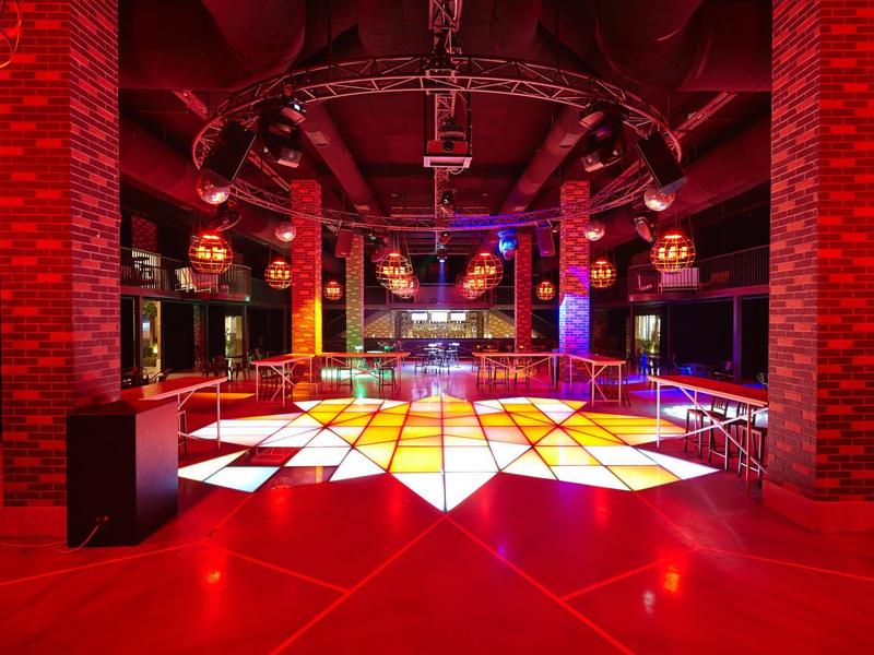 Club moderno con pista de baile iluminada y paredes interiores de ladrillo rojo.