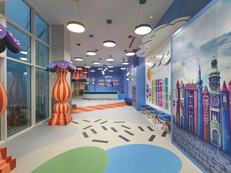 Pasillo colorido del hotel con esculturas de hongos y un mural de una vista de la ciudad.