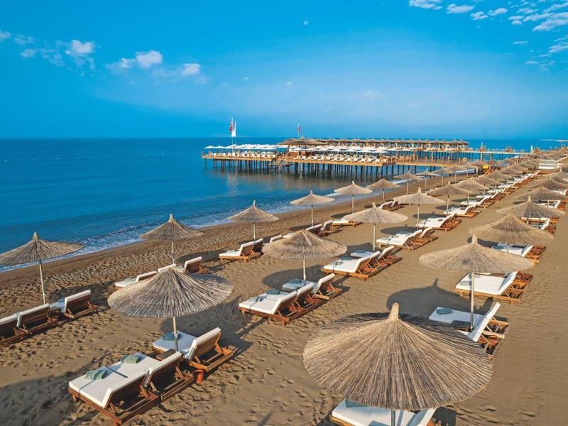 Playa con tumbonas y sombrillas junto a un mar tranquilo bajo un cielo azul.