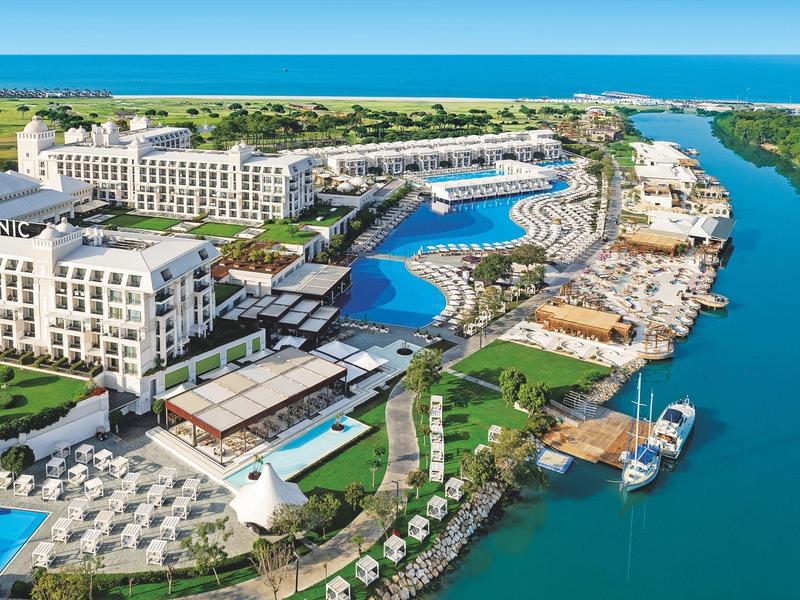 Resort de lujo con grandes piscinas, tumbonas y muelles para barcos junto a un río.