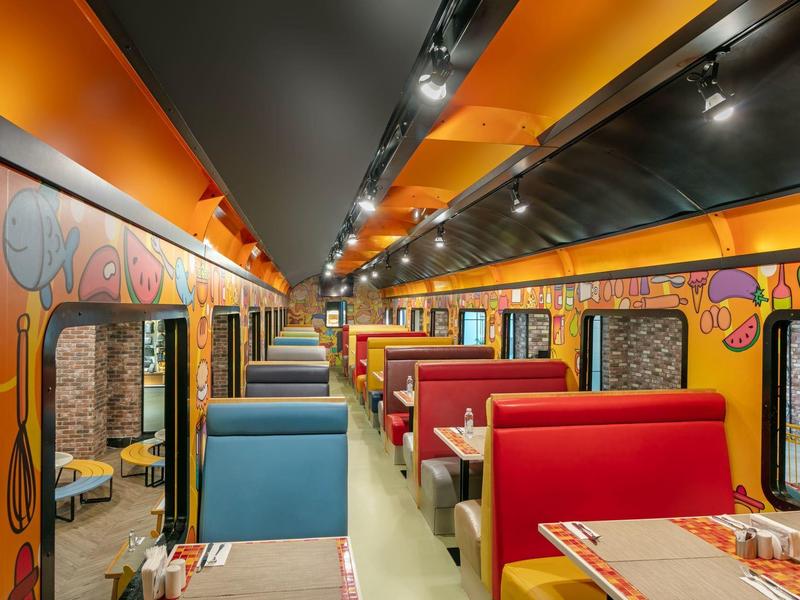 Vagón comedor colorido con asientos de colores y murales vibrantes dentro de un tren.