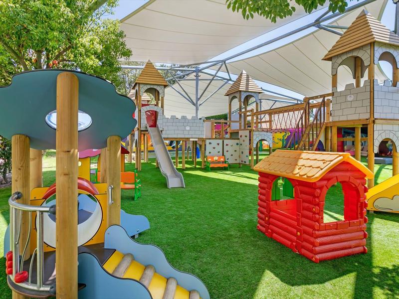 Área de juegos infantiles colorida con toboganes, estructuras para escalar y una pequeña casita de juego al aire libre.