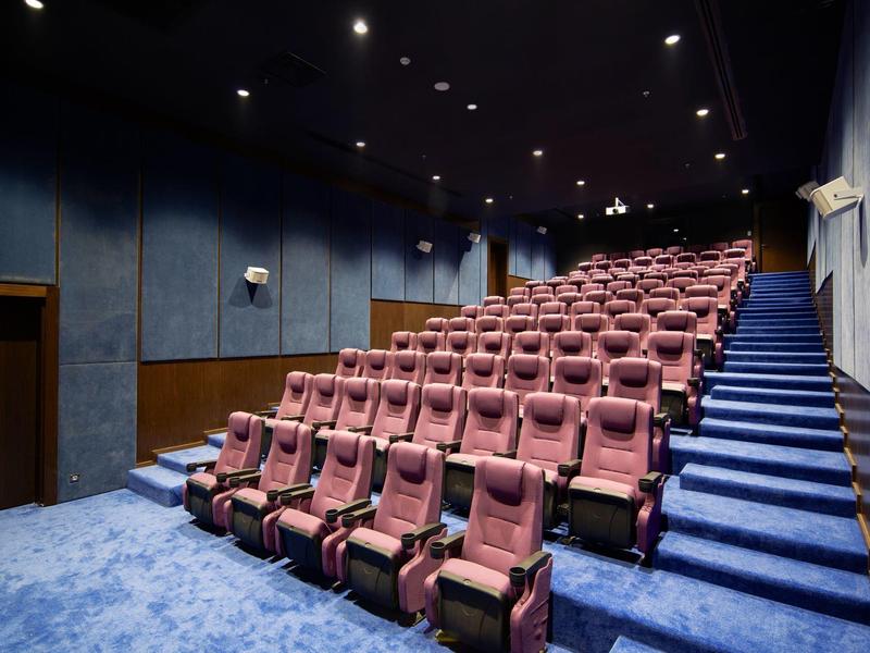 Una sala de cine moderna con asientos rojos y paredes y alfombra azules.