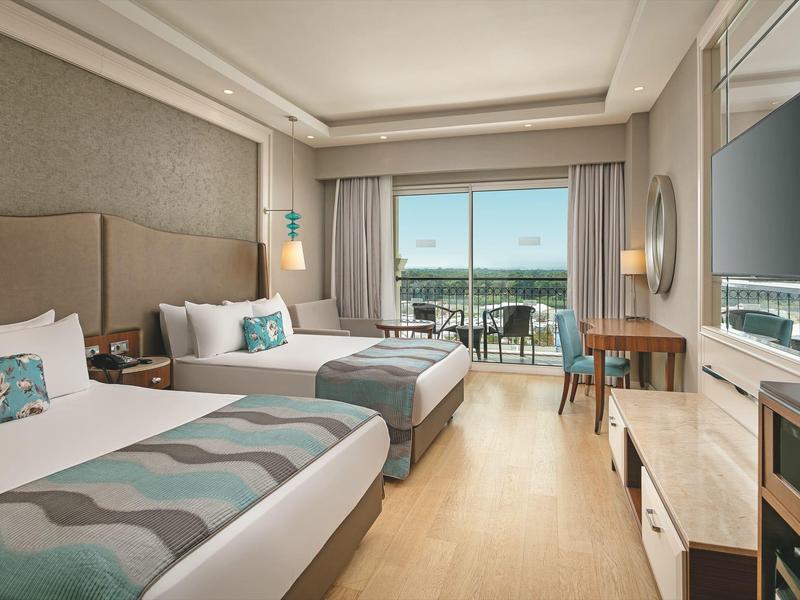 Habitación de hotel moderna con dos camas, escritorio, televisor y balcón con vista al mar.