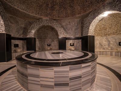 Kruhová kamenná fontána v historickém hammamu s klenutými kamennými zdmi a oblouky.