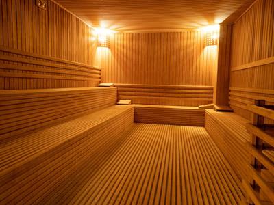 Interiér dobře osvětlené sauny s dřevěnými lavicemi a zdroji tepla na stěně.