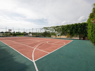 Campo da tennis vuoto con recinzione verde e alberi sullo sfondo sotto cielo nuvoloso