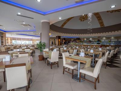 Prostorná moderní jídelna s mnoha bílými židlemi a dřevěnými stoly pod osvětleným stropem.