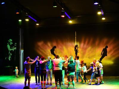 Gruppo di persone in piedi insieme su un palcoscenico con illuminazione colorata.