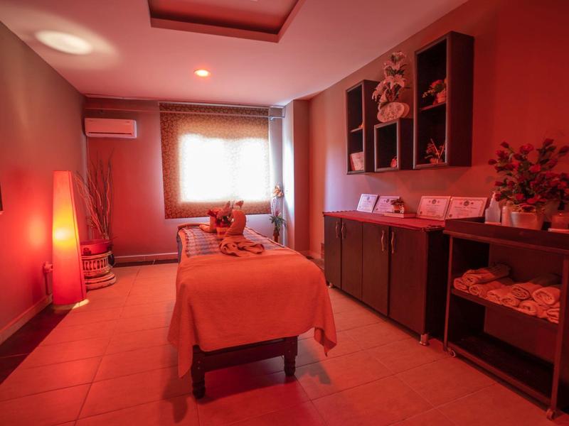 Útulná masážní místnost s teplým červeným osvětlením a masážním stolem pokrytým prostěradly.