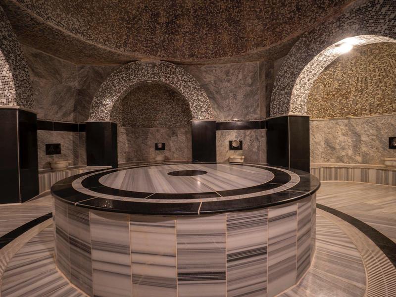 Kruhová kamenná fontána v historickém hammamu s klenutými kamennými zdmi a oblouky.