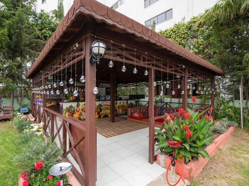 Otevřený pavilon s dřevěnými sloupy a dekoracemi v zelené zahradě hotelu.