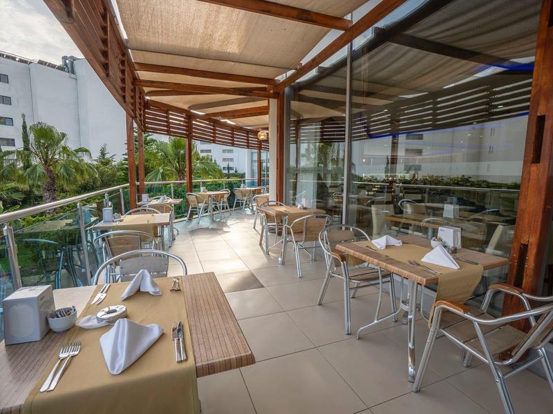 Moderní venkovní prostor hotelové restaurace se prostřenými stoly a výhledem na okolní budovy.