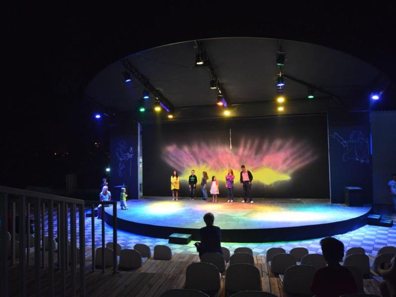 Pódium s tanečníky a barevným pozadím na noční venkovní akci.