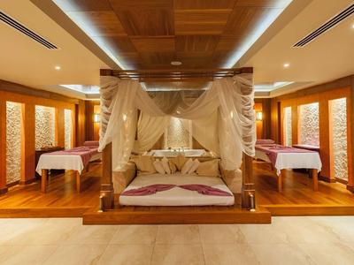 Luxe hotelkamer met hemelbed en twee eenpersoonsbedden in warme houtdecoratie.