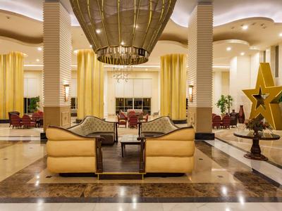 Elegante hotel lobby met gele fauteuils, hoge plafonds en grote verlichting.