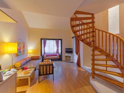 Gezellige hotelkamer met wenteltrap, bank, tv en groot raam met gordijnen.