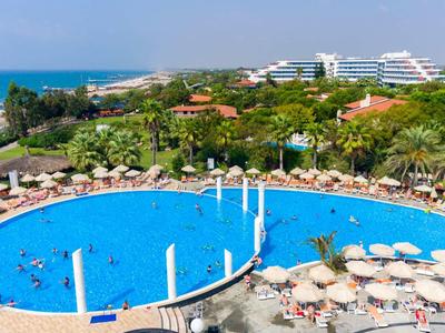 Grande piscina dell'hotel con ombrelloni e lettini, area verde e mare sullo sfondo.