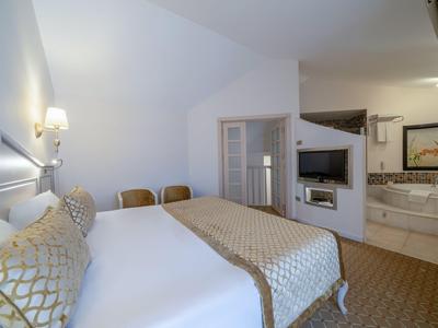 Helles Hotelzimmer mit zwei Betten, Sitzgelegenheiten und offenem Bad mit Badewanne.