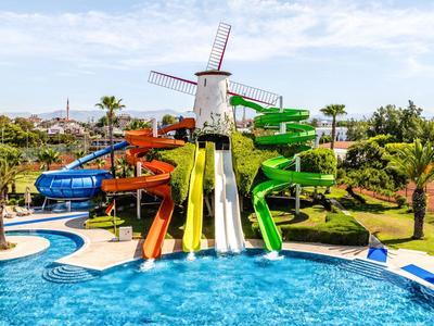 Bunter Wasserrutschenkomplex vor einem Windmühlengebäude mit Pool und Palmen rundherum.