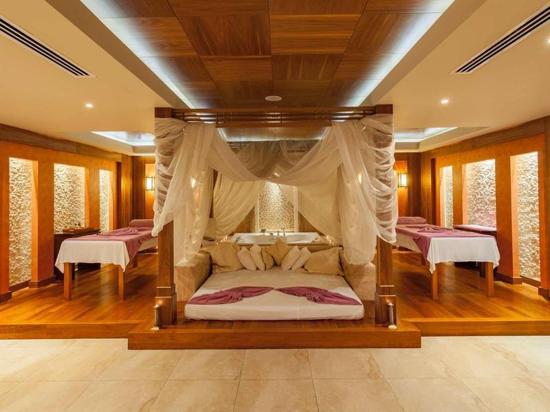 Luxe hotelkamer met hemelbed en twee eenpersoonsbedden in warme houtdecoratie.