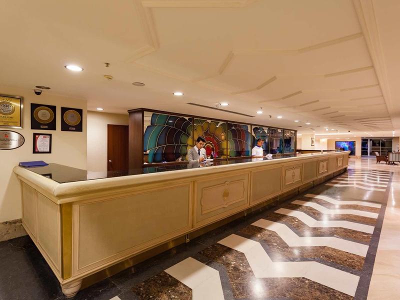 Een lange receptiebalie in een hotelhal met marmeren tegelvloer en decoratieve wand.