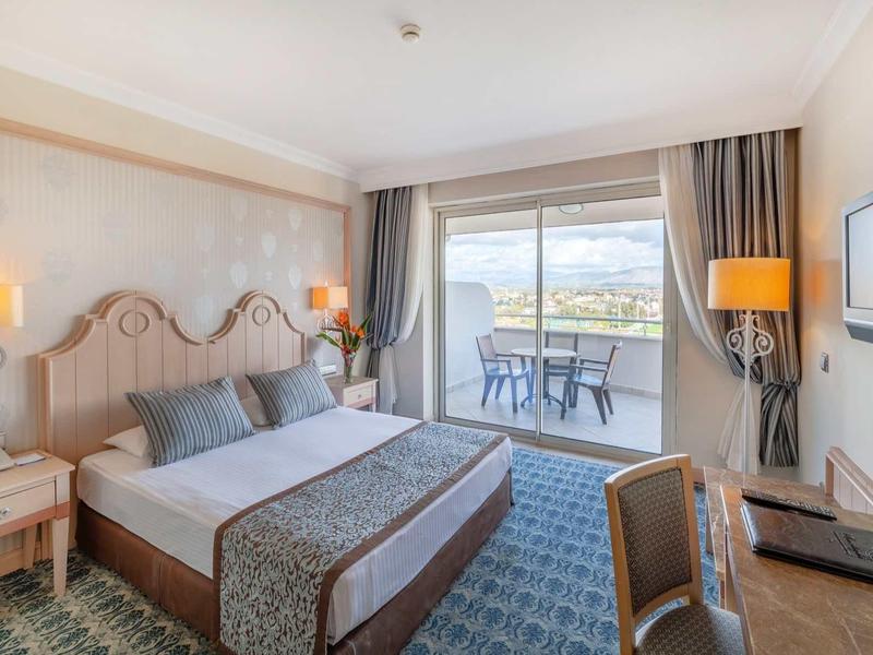 Licht hotelkamer met tweepersoonsbed, balkon en uitzicht op het landschap.