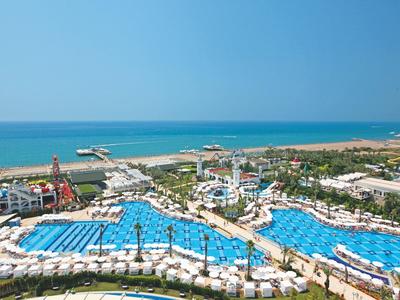 Großer Hotelpool mit vielen Liegestühlen und Blick auf das blaue Meer unter klarem Himmel.