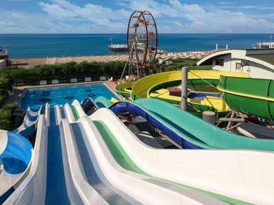 Bunte Wasserrutschen im Freibad mit Meer und Strand im Hintergrund unter blauem Himmel.
