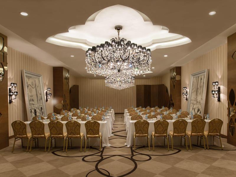 Elegantní banketní sál s velkým lustrem a řadami židlí kolem dlouhého stolu připraveného k jídlu