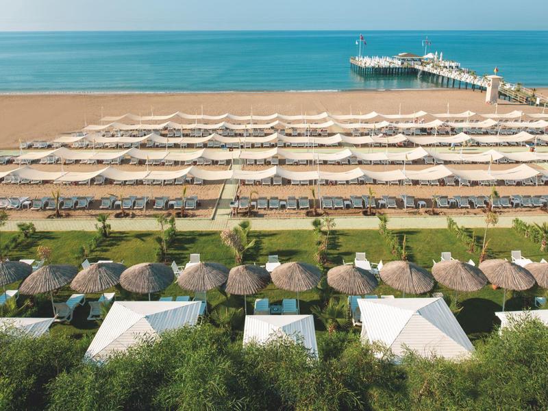 Pláž s deštníky a lehátky u moře a dřevěné molo, které zasahuje do vody.