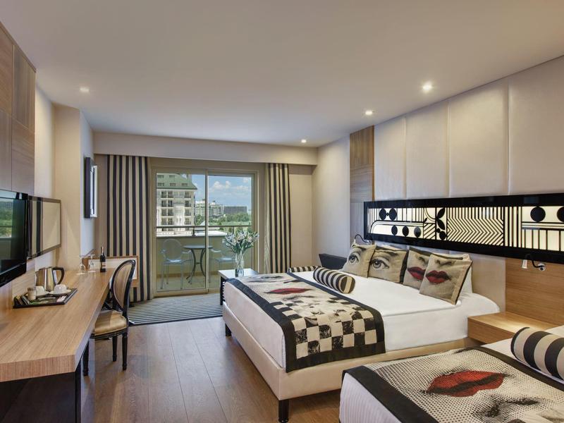 Moderní hotelový pokoj s postelí, stolem, TV a balkonem s výhledem na vodu.