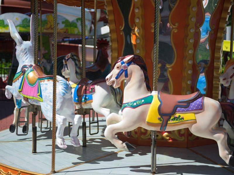 Barevní historické kolotočoví koně na kulaté plošině pod dřevěnou střechou.