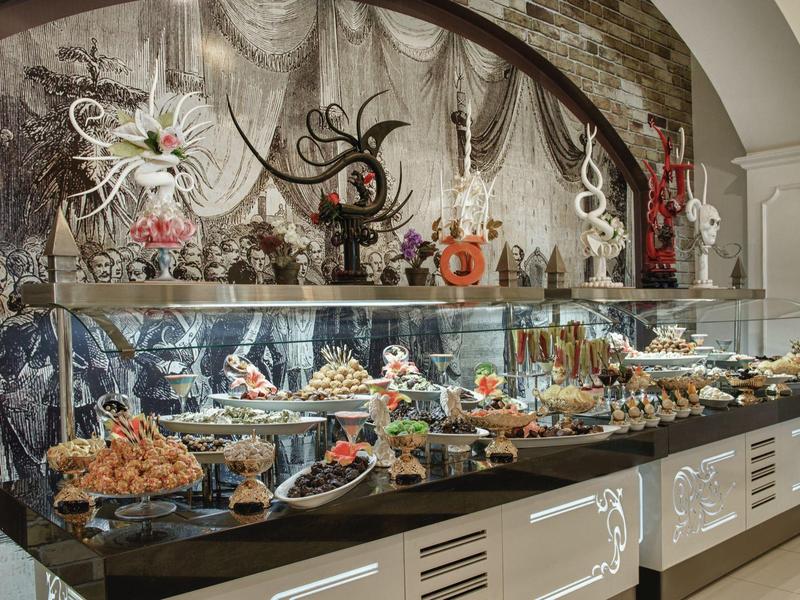 Elegantní dezertní bufet s různými pečivy a uměleckými cukrovými dekoracemi v stylovém hotelovém prostředí.