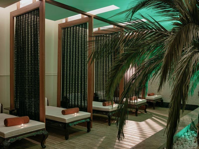 Zastíněná venkovní odpočinková část s polstrovanými křesly a tropickými rostlinami pod zelenou střechou.