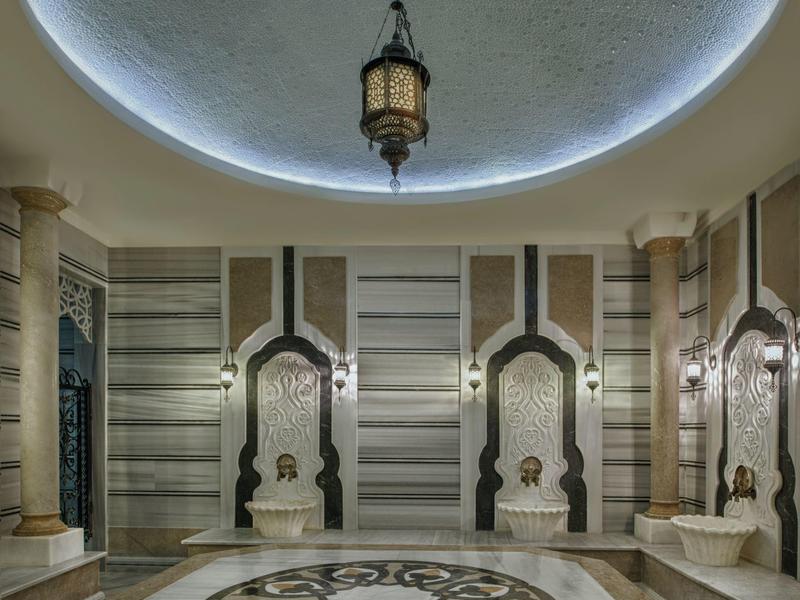 Elegantní lázeňská místnost s ozdobnými mramorovými stěnami, dekorativní podlahou a zavěšenou lucernou uprostřed.