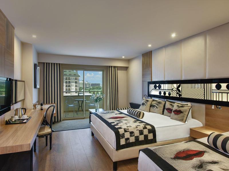 Moderní hotelový pokoj s manželskou postelí, balkonem, TV, psacím stolem a elegantním osvětlením.