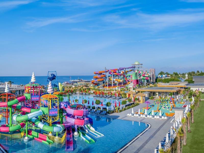 Barevný vodní park s tobogány a bazény vedle hotelového areálu za slunečného dne.