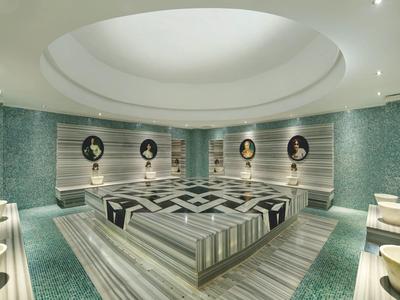Großer türkischer Hamam mit Marmorliegen, runden Wänden und runden Spiegeln an grünen Kacheln.