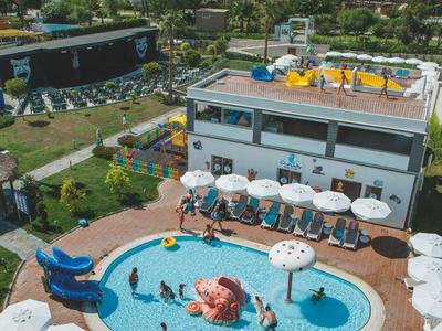 Ein Hotelpool mit blauer Wasserrutsche, vielen weißen Sonnenschirmen und Meer im Hintergrund.