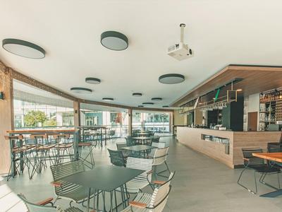 Moderne Cafeteria mit vielen Tischen, Stühlen, großen Fenstern und heller, offener Atmosphäre.