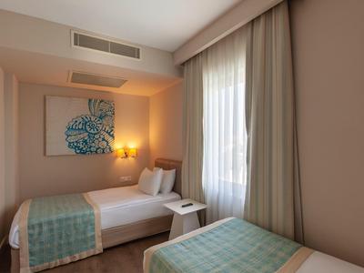 Kleines Schlafzimmer mit zwei Einzelbetten, großen Fenstern, hellen Wänden und moderner Wanddekoration.