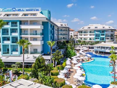 Modern hotel met groot buitenzwembad, ligstoelen en palmbomen onder een blauwe lucht.