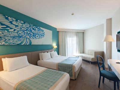 Lichte hotelkamer met twee eenpersoonsbedden, bureau en zithoek onder een groot raam.