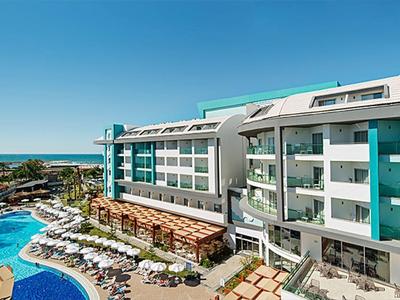 Modernes Hotel mit großen Glasfronten, Poollandschaft, Liegestühlen und Blick auf das Meer im Hintergrund.