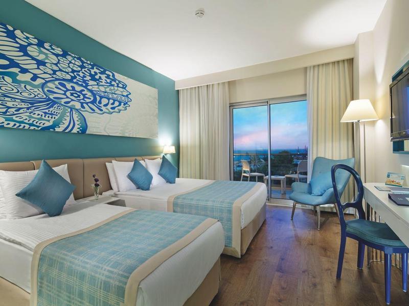 Modern hotelkamer met twee bedden, bureau, stoelen en groot raam met uitzicht.