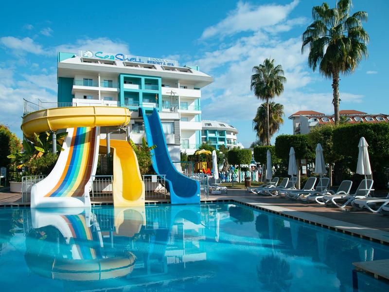 Hotelzwembad met kleurrijke glijbanen, parasols en palmbomen onder een blauwe lucht.