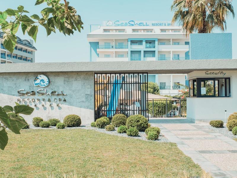 Moderne hotelentree met tuin en hotelgebouw op de achtergrond bij zonnig weer.