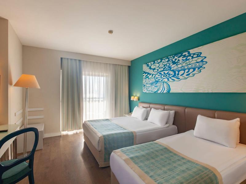 Hotelkamer met een tweepersoons- en een eenpersoonsbed, houten vloer en turquoise wanddecoratie.