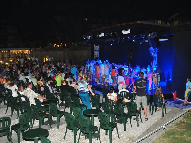 Buitenevenement 's nachts met publiek, podium, kleurrijke lichten en stoelen.